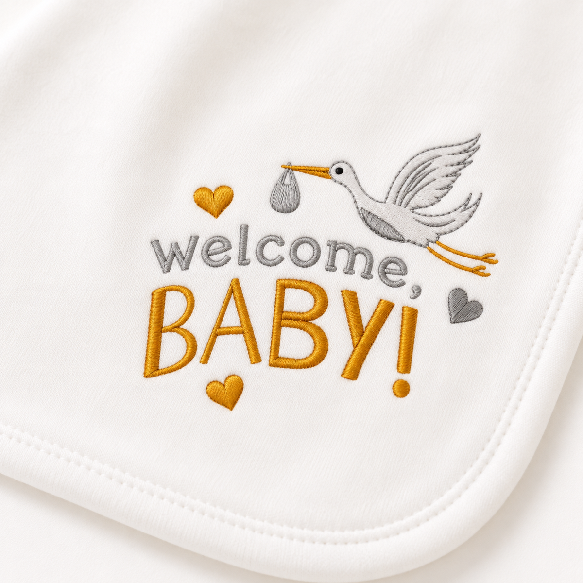 Close-up of the "Welcome, Baby!" stork embroidery detail on an organic baby blanket in soft grey and gold thread